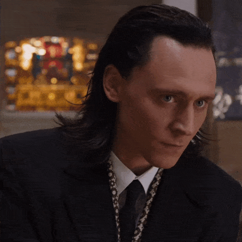 a man with long hair wearing a black suit and tie