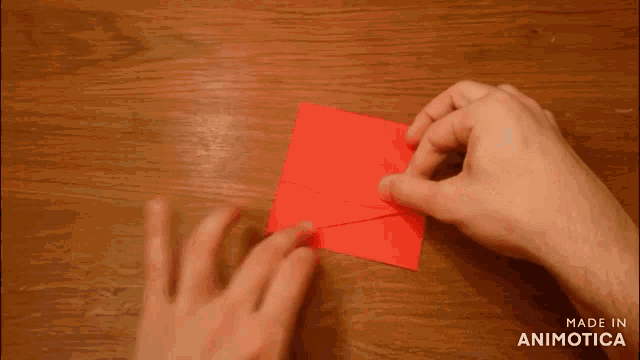 a person is folding a red piece of paper on a wooden table ..