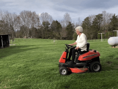 an older woman is riding a lawn mower in a field