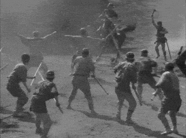 a black and white photo of a group of men fighting with sticks