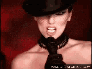 a woman is singing into a microphone wearing a top hat and choker .