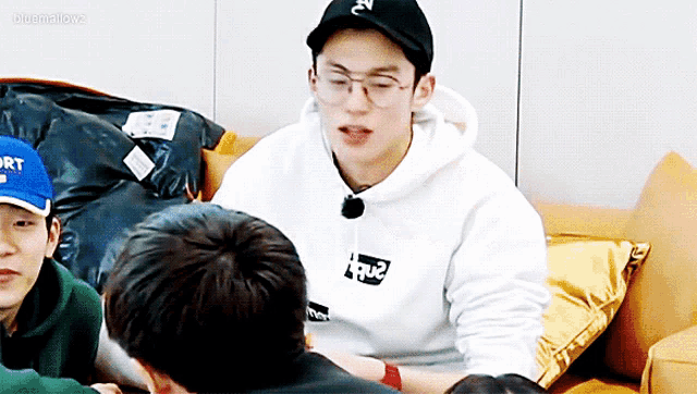 a man wearing a white sweatshirt with the word supreme on it sits on a couch