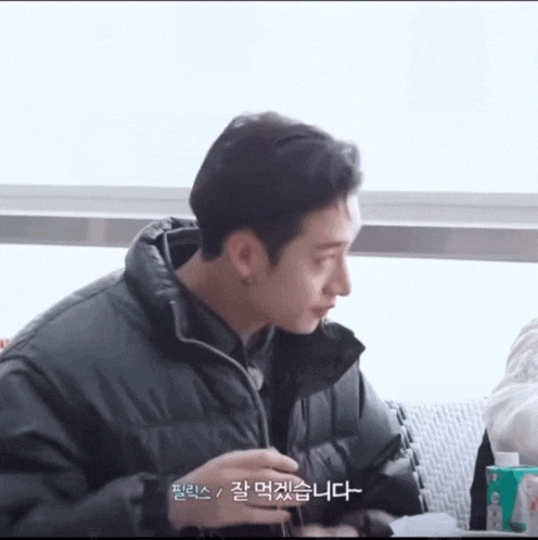 a man in a black jacket is sitting on a couch with a foreign language written on his face