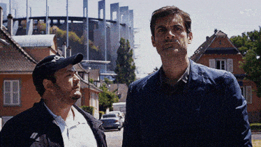 two men standing next to each other in front of a building that says tv on the bottom