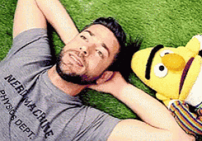 a man is laying on the grass next to a stuffed sesame street character named bert
