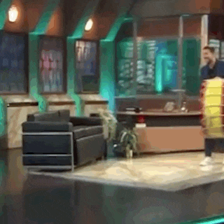 a man is standing on a stage in a room with a couch and a desk .