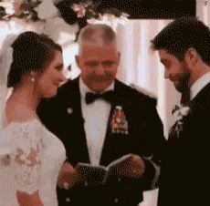 a bride and groom are standing in front of a man in a suit