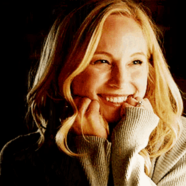 a woman with blonde hair is smiling with her hands on her chin