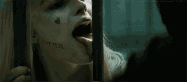 a woman with a tattoo on her face is laughing in a jail cell behind bars .