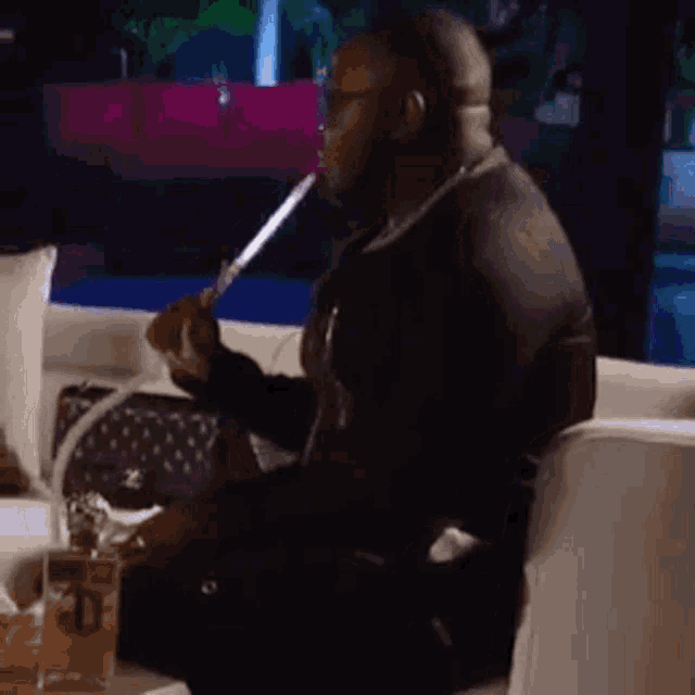 a man wearing a face mask is sitting on a couch drinking from a bottle .