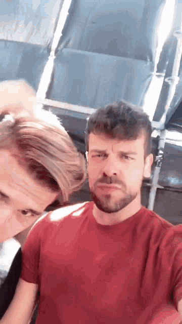 a man in a red shirt is standing next to another man with a beard