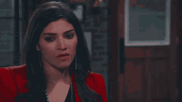 a woman in a red jacket and black top is standing in front of a door .