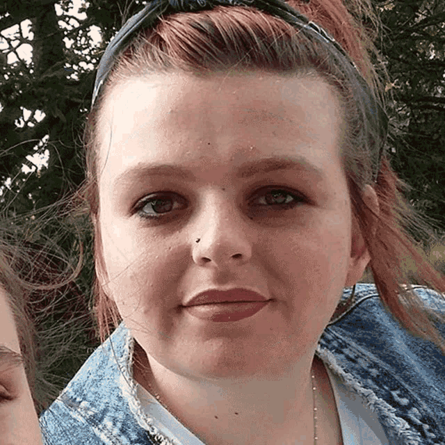 a woman wearing a headband and a denim jacket is looking at the camera .