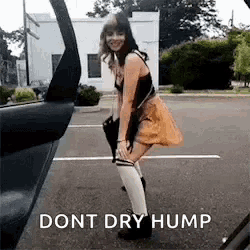 a woman in a skirt and knee high socks is standing in a parking lot next to a car .