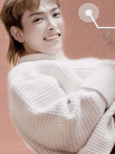 a young man wearing a white sweater and a mullet is smiling and looking at the camera .