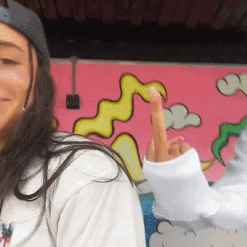 a woman giving the middle finger in front of a colorful mural