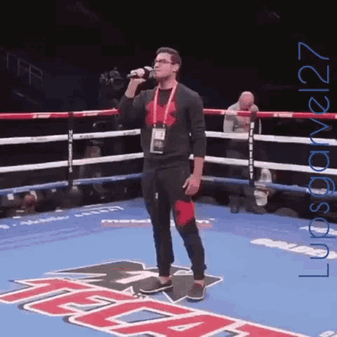 a man sings into a microphone in a boxing ring with the word tecate on the floor