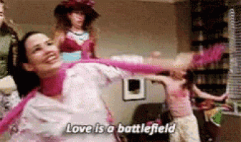 a woman is dancing in a room with the words love is a battlefield written on the screen .