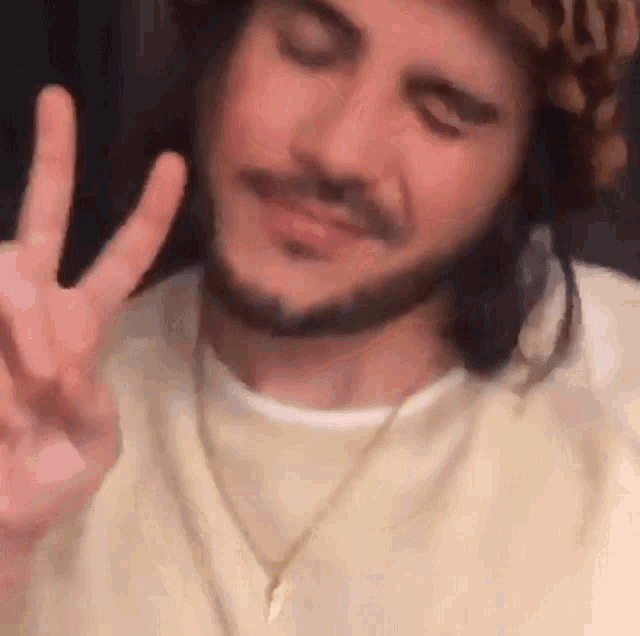 a man with a beard is wearing a hat and making a peace sign .