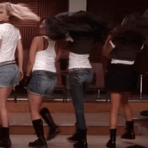 a group of women are dancing on a stage and one of them is wearing a white tank top