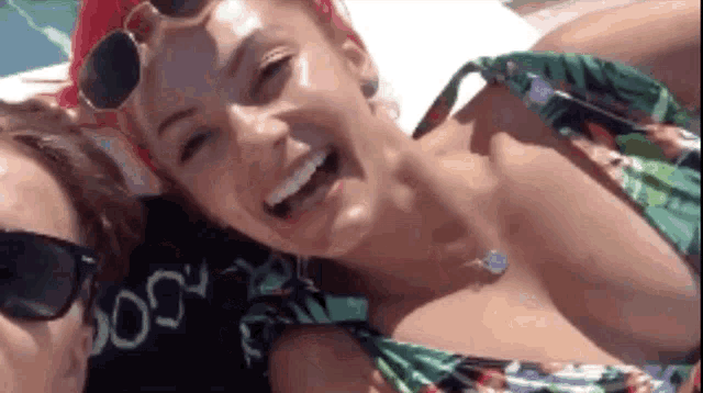 a woman in a bikini and sunglasses is smiling for the camera while laying on a beach .