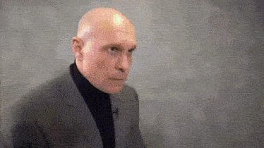a bald man wearing a suit and turtleneck is making a funny face .