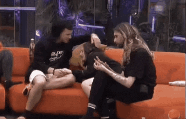a group of people are sitting on an orange couch and one of them is wearing a shirt that says " ego " on it