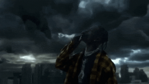 a man with dreadlocks is standing in front of a cloudy sky looking up .