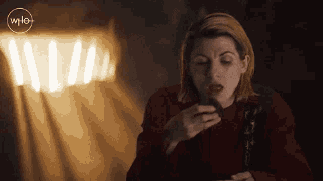 a woman in a red sweater is eating a piece of food in front of a sign that says who