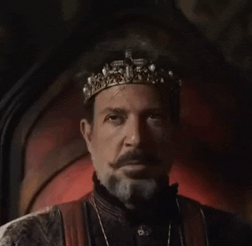 a man with a beard and mustache is wearing a crown and sitting on a throne .