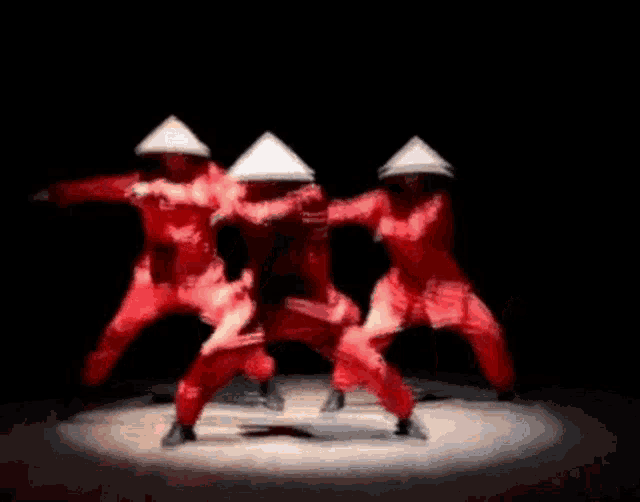 a group of people wearing red jumpsuits and conical hats are dancing on a stage .