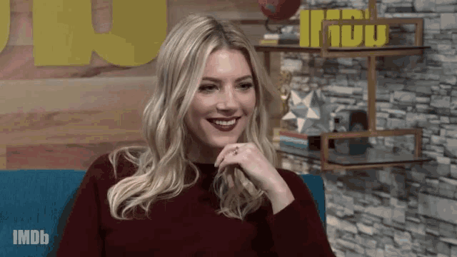a woman in a red sweater is smiling in front of an imdb sign