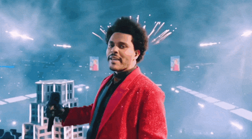a man in a red suit is holding a microphone in front of fireworks