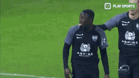 two soccer players wearing aspire academy jerseys are walking on the field