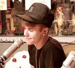 a young man wearing a baseball cap and earbuds is sitting in front of a microphone .