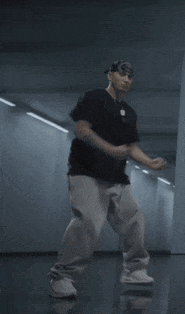 a man in a black shirt and grey pants is dancing in a dark room