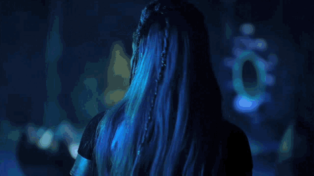 a woman with blue hair is standing in front of a blue light