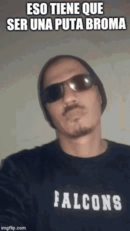 a man wearing sunglasses , a beanie and a falcons t-shirt is making a funny face .