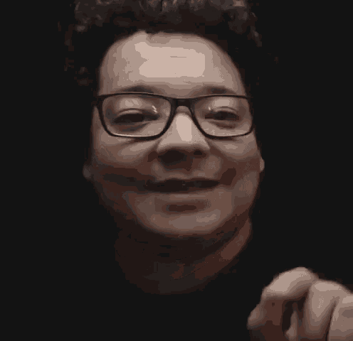 a man wearing glasses and a black shirt is smiling in a black background .