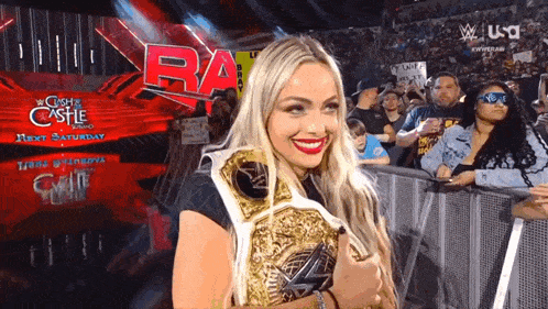 a woman is holding a wrestling championship belt in front of a crowd at a wrestling show