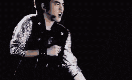 a man is singing into a microphone while wearing a sequined jacket .