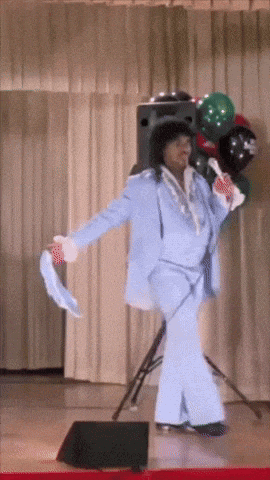a woman in a blue suit is dancing on a stage with balloons in the background