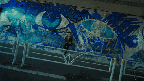 a man is standing in front of a wall with a blue and white painting on it