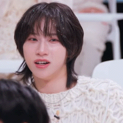 a woman with short brown hair is wearing a white sweater and looking at the camera .