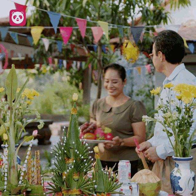a man and woman standing in front of a table with flowers and a panda logo