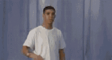a man in a white t-shirt is standing with his arms outstretched in front of a blue curtain .