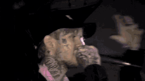 a man with a beard and a pink shirt is standing in the dark .