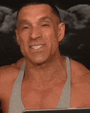 a man in a grey tank top is smiling