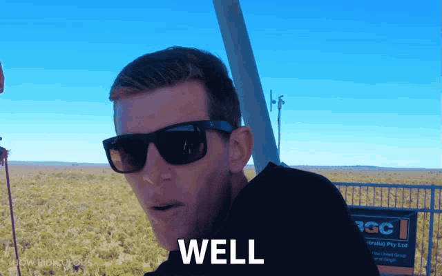 a man wearing sunglasses says well in front of a sign that says rgc