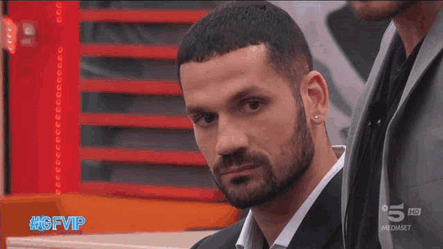 a man with a beard and ear piercings is on a television screen with the hashtag #gfvip